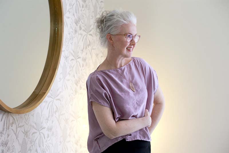 rini wearing a light purple silk top with a feather necklace