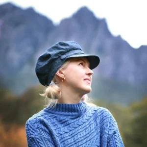 Rini standing in front of Mount Roland wearing a blue hat and cashmere sweater